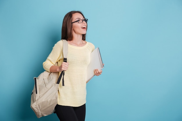 Belle fille souriante avec sac à dos et ordinateur portable isolé sur fond bleu