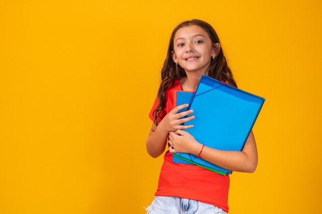 Belle fille souriante tenant un livre allant à l'école. gros plan portrait, fond jaune isolé, enfance. enfant étreignant un livre. mode de vie, intérêt, passe-temps, temps libre, temps libre