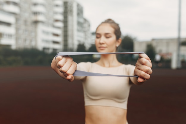 Une belle fille avec un sourire fléchit ses muscles Étire les trains avec une bande élastique