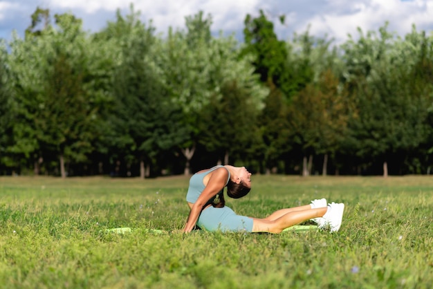 Une belle fille sportive en tenue de sport pratique le yoga sur l'herbe verte dans le parc de la ville. Acrobate dans la pose de flexion arrière, corps flexible fort de gymnastique de fille