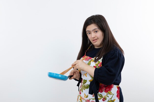 Belle fille en tablier coloré se prépare pour la cuisson avec une cuillère et une casserole.