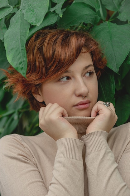 Une belle fille de taille plus aux cheveux rouges parmi les branches vertes de plantes tropicales