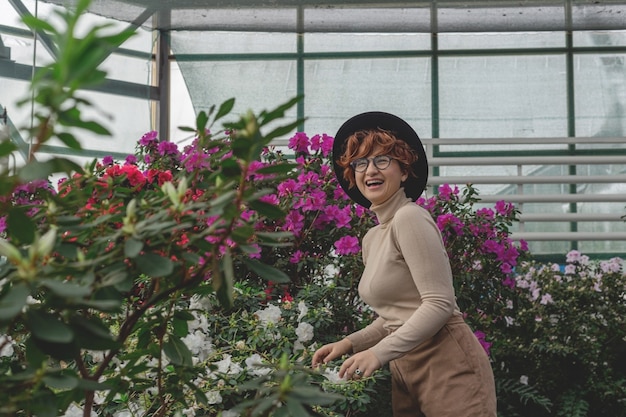 Une belle fille de taille plus dans un chapeau rit parmi les plantes vertes de serre