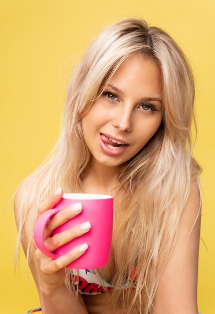 Belle fille tenant une tasse rose sur fond jaune, en studio