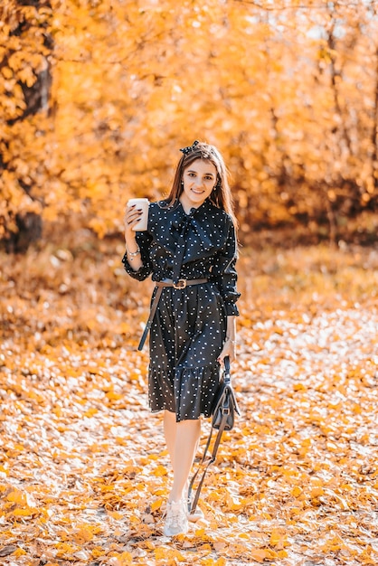 Belle fille tenant un verre de café par une journée ensoleillée d'automne