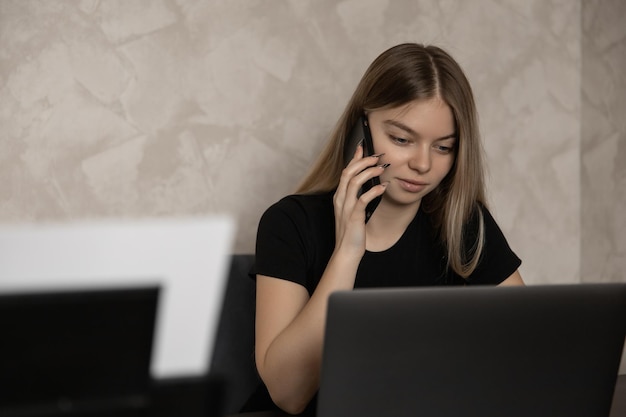 Belle fille travaillant à distance à la maison à l'ordinateur et parlant au téléphone