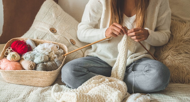 Belle fille tricote un pull chaud sur le lit. Tricoter comme passe-temps. Accessoires pour tricot.