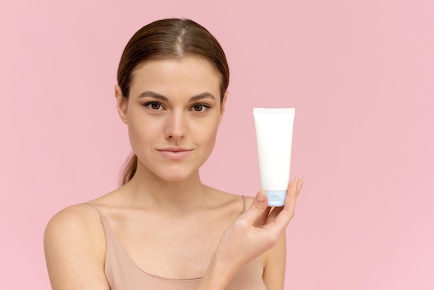 Belle fille avec un tube de crème hydratante sur fond rose regarde la caméra Place pour la conception de votre produit cosmétique