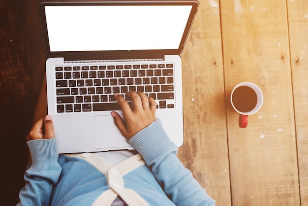 Belle fille a utilisé un ordinateur portable et une tasse de café dans les mains de la fille assise sur un plancher en bois