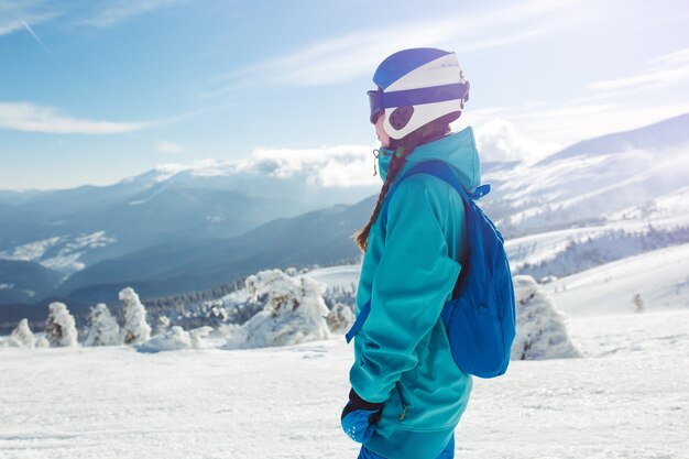 Une belle fille en vêtements d'hiver, un casque bleu et une veste verte passe un bon moment dans les montagnes.