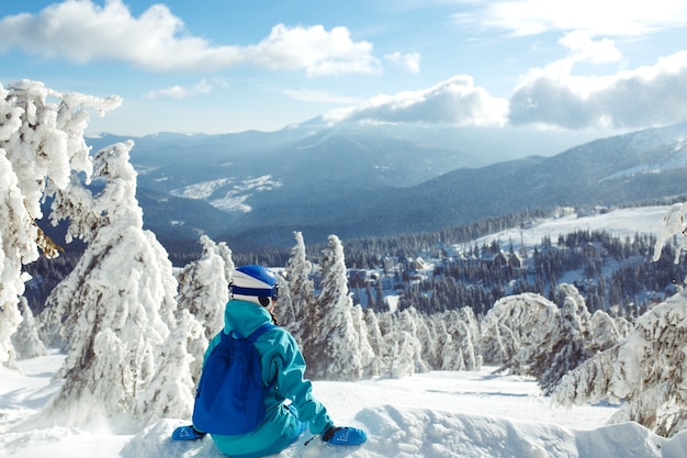 Une belle fille en vêtements d'hiver, un casque bleu et une veste verte passe un bon moment dans les montagnes.