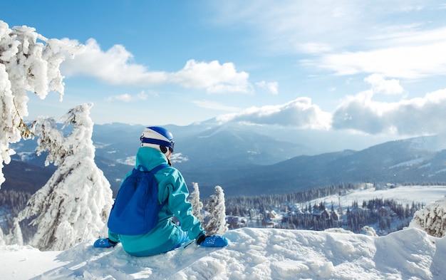 Une belle fille en vêtements d'hiver, un casque bleu et une veste verte passe un bon moment dans les montagnes.