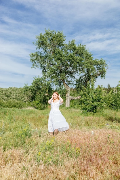 Belle fille vêtue d'une robe blanche avec des fleurs dans un champ avec vue sur le ciel