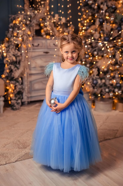 Belle fille vêtue d'une robe élégante sur fond de lumières de Noël et d'un arbre de Noël dans un bel intérieur