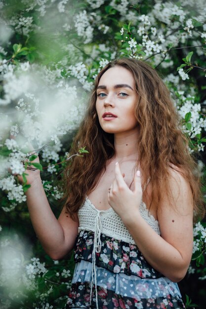 Une belle fille vêtue d'une robe se tient à côté d'un bus de cerisiers en fleurs