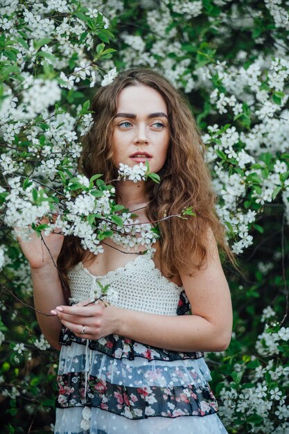 Une belle fille vêtue d'une robe se tient à côté d'un bus de cerisiers en fleurs