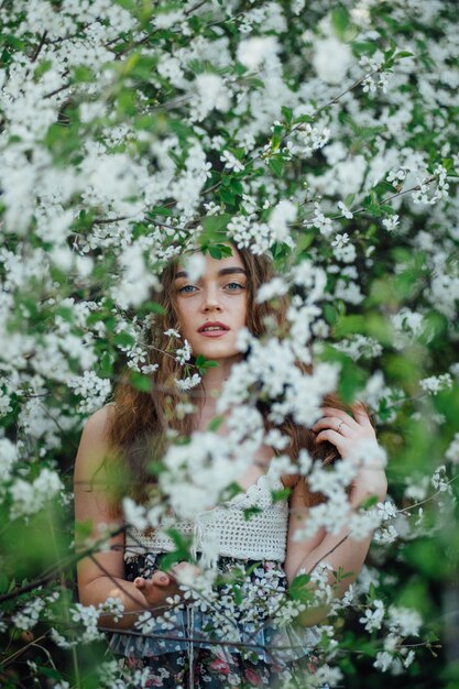 Une belle fille vêtue d'une robe se tient à côté d'un bus de cerisiers en fleurs