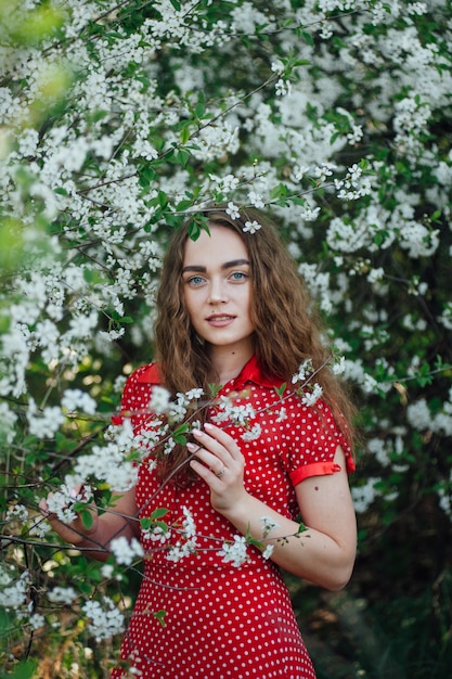 Une belle fille vêtue d'une robe se tient à côté d'un bus de cerisiers en fleurs