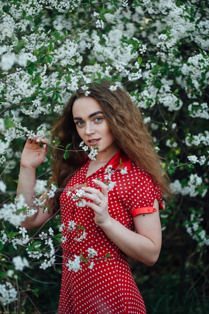 Une belle fille vêtue d'une robe se tient à côté d'un bus de cerisiers en fleurs