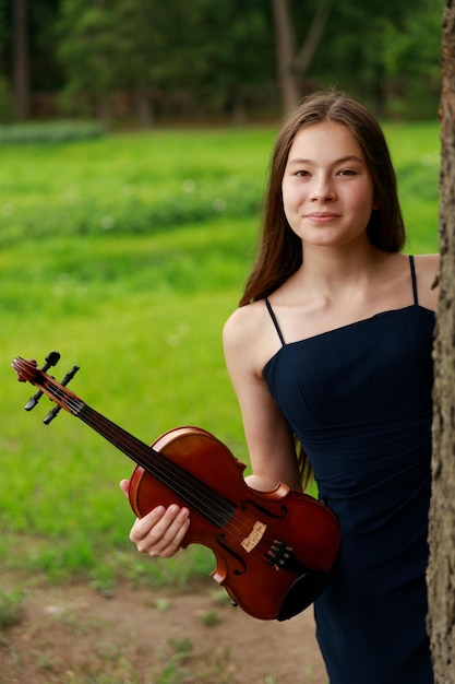 Belle fille avec violon, jetant un coup d'œil derrière un arbre