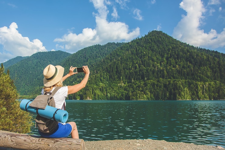 Photo belle fille voyageur prend des photos d'un grand lac de montagne bleue à l'arrière-plan des montagnes