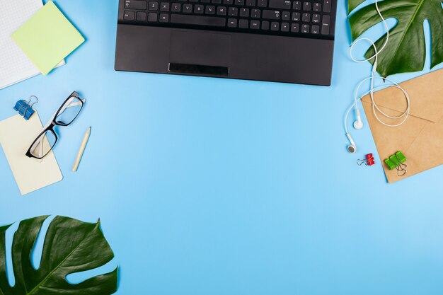 Belle flatlay avec un ordinateur portable, des lunettes, des feuilles de philodendron et d'autres accessoires professionnels. Concept d'un bureau à domicile. Mise à plat.