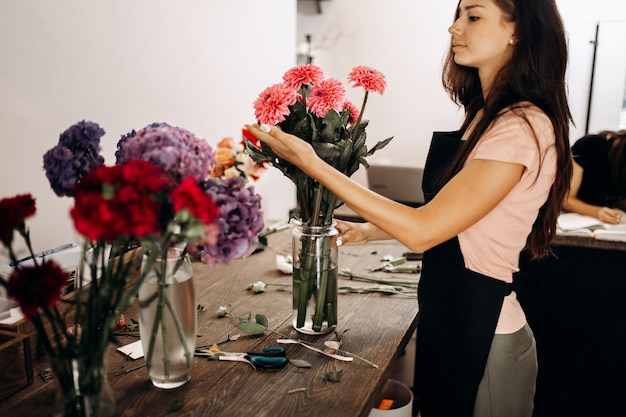 Une belle fleuriste en tablier noir touche un chrysanthème rose dans un vase.