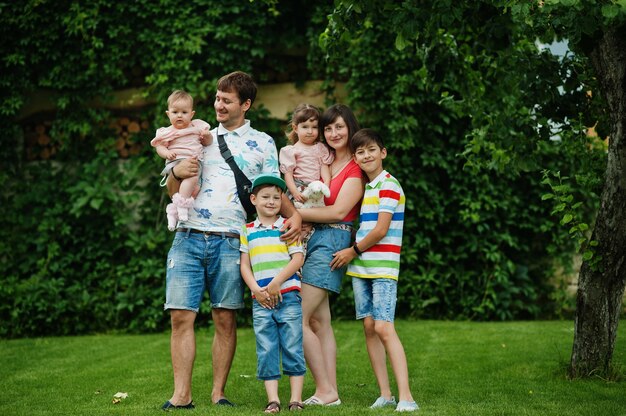 Belle grande famille avec de jeunes parents et quatre enfants se tiennent dans l'herbe verte de la cour.