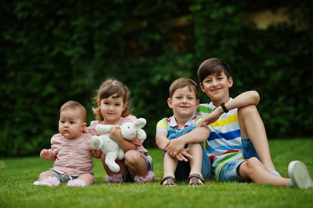 Belle grande famille avec quatre enfants assis dans l'herbe verte à la cour.