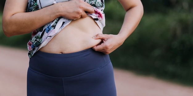 Belle grosse femme avec ruban à mesurer Elle utilise sa main pour presser l'excès de graisse isolé sur fond blanc Elle veut perdre du poids le concept de chirurgie et décomposer la graisse sous le