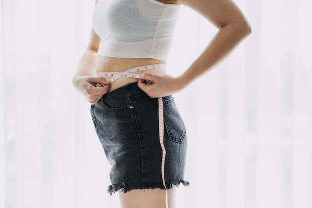 Belle grosse femme avec ruban à mesurer Elle utilise sa main pour presser l'excès de graisse isolé sur fond blanc Elle veut perdre du poids le concept de chirurgie et décomposer la graisse sous le