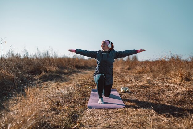 Belle grosse femme en vêtements de sport pratique le yoga asana par une journée ensoleillée dans un parc d'automne, femme sportive heureuse s'entraînant en plein air.