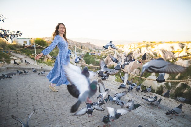 Une belle et heureuse fille vêtue d'une robe et de nombreux pigeons dans les montagnes de Cappadoce