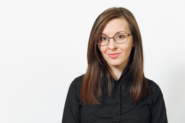 Belle heureuse jeune femme d'affaires aux cheveux bruns souriante en chemise classique noire et lunettes isolées sur mur blanc