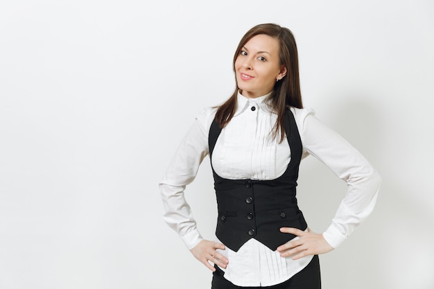 Belle heureuse jeune femme d'affaires aux cheveux bruns souriante en costume noir, chemise blanche à la recherche d'une caméra isolée sur un mur blanc