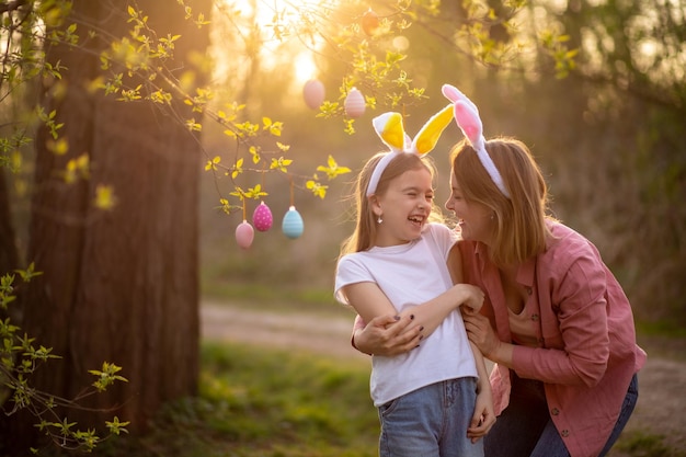 Belle et heureuse maman et sa fille dans des oreilles de lapin décorent l'arbre avec des oeufs de pâques famille heureuse célébrant pâques