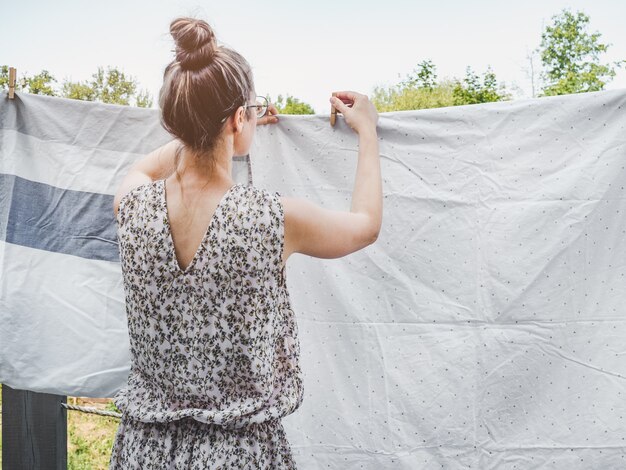 Belle hôtesse accroche le linge de lit avec des arbres verts par une journée claire et ensoleillée