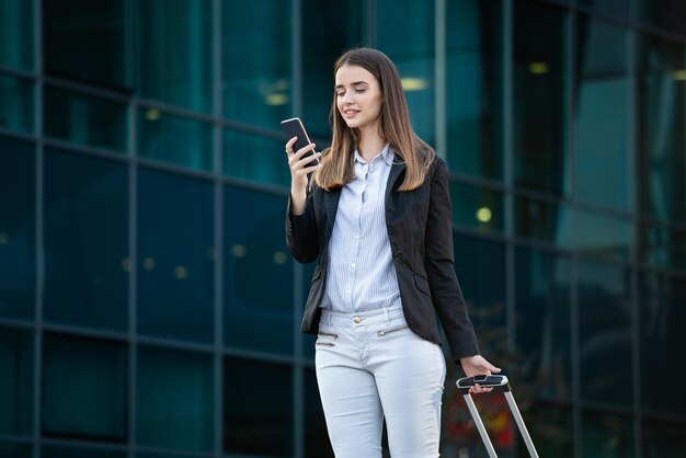 Une belle hôtesse de l'air souriante qui porte des bagages en route pour l'avion à l'aéroport Une femme d'affaires à l' aéroport international qui regarde son téléphone portable