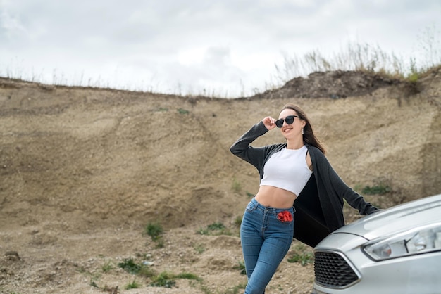 Belle jambe près de la voiture posant sur le rivage sablonneux pendant les vacances d'été