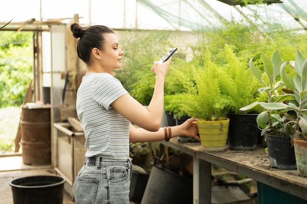 Belle jardinière adolescente en tenue décontractée prend une photo de plantes au téléphone pour un blog.