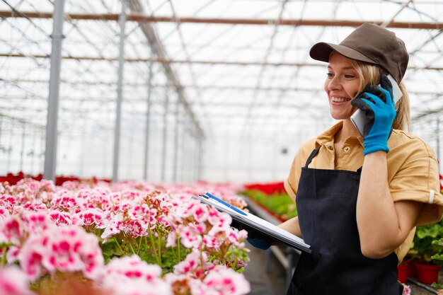 Belle jardinière femme parlant au téléphone avec un client et prend des notes en serre