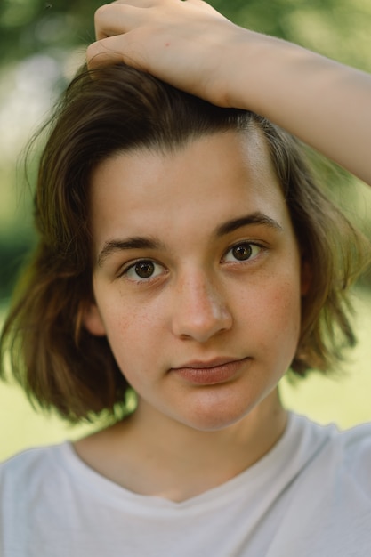 Belle jeune adolescente aux cheveux bob à la mode dans un t-shirt blanc en plein air et regardant c...