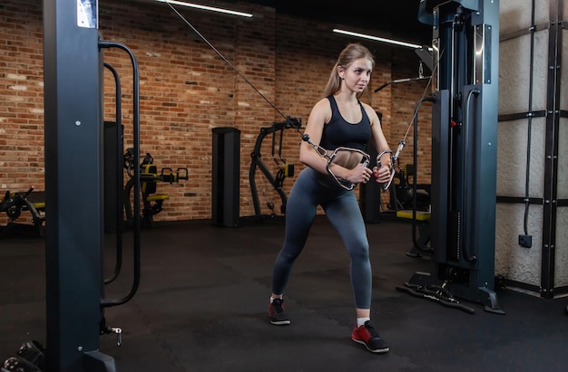 Belle jeune athlète féminine caucasienne exerçant avec une machine de croisement de câbles dans une salle de fitness.