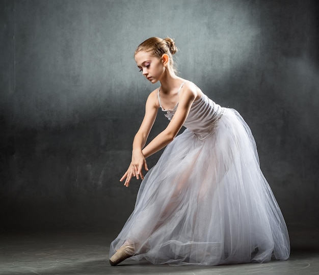 Belle jeune ballerine danse en studio sur fond sombre Une petite danseuse Danseuse de ballet
