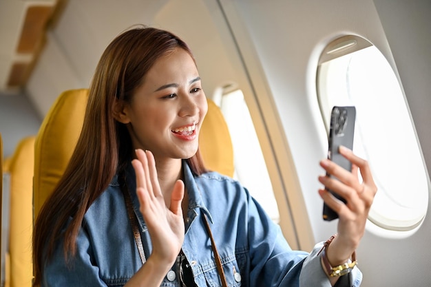 Belle jeune blogueuse de voyage asiatique s'enregistrant avec un smartphone pendant le vol