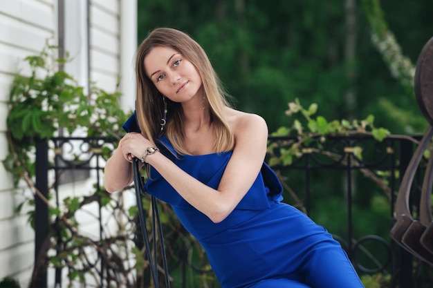 belle jeune blonde en salopette bleue est assise sur le balcon pendant la saison chaude