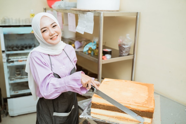 Belle jeune boulanger faisant des gâteaux dans sa cuisine. jeune fabricant de gâteau musulman asiatique