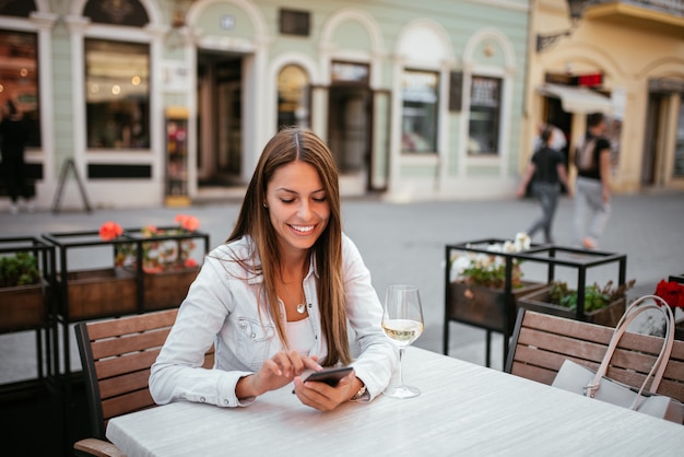 Belle jeune brune à l&#39;aide de téléphone assis dans le restaurant en plein air.