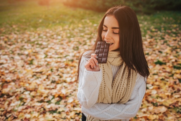 Belle jeune brune assise sur une feuille d'automne tombée dans un parc