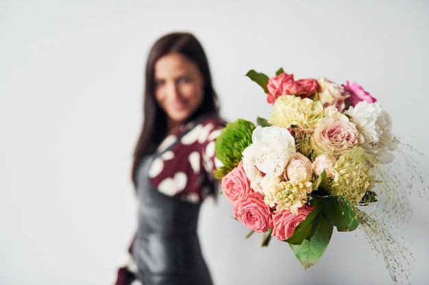 Belle jeune brune en jupe noire debout à l'intérieur sur fond blanc avec bouquet dans les mains